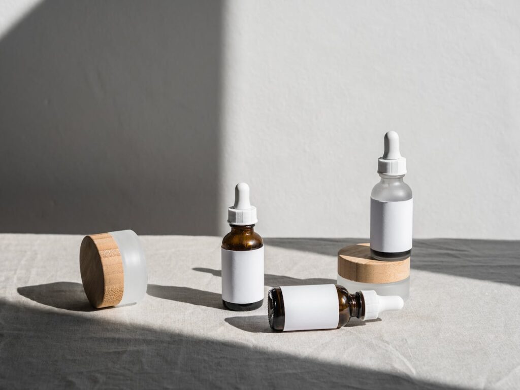 Minimalist composition of beauty bottles with droppers and containers on fabric under natural lighting.